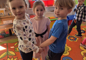 Jagoda, Felicja i Józio stoją w kółeczku na dywanie i trzymają się za ręce, tańczą w trójkę do piosenki.