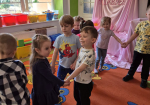 Wiktoria, Wojtek i Dawid tańczą w trójkę na dywanie trzymając się za ręce.