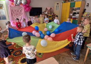 "Motylki" w trakcie zabawy z chustą, na której widać różowe i niebieskie balony.