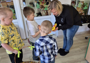 Filip, Karol i Krzyś składają życzenia cioci Małgosi z grupy "Biedronek" i wręczają słodki upominek w kształcie cyfry 8 z cukierkiem w środku.