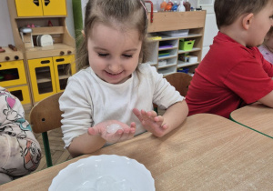 Wiktoria siedzi przy stoliku i trzyma w dłoni kostkę lodu.