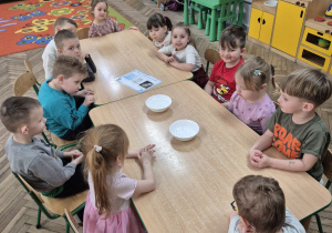 Dzieci z grupy "Motylki" siedzą przy stoliku, na którym stoją dwie białe miski, w jednej z nich jest woda, w drugiej kostki lodu.