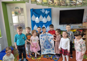 Dzieci stoją na tle dekoracji, Filip, Wojtek, Krzyś i Felicja trzymają skończoną pracę plastyczną.