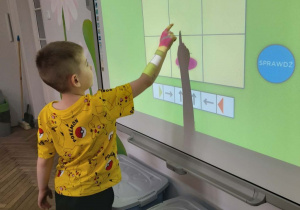Mikołaj stoi przed tablicą multimedialną i prowadzi motyla na planszy zgodnie z podanym kodem.