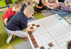 Oskar układa na macie brązowe kwadraty według podanego kodu.