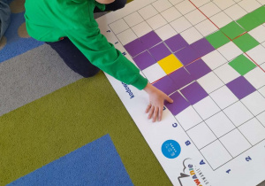 Hubert układa z fioletowych kwadratów kwiatek wiosenny na macie do kodowania.