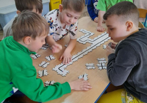 Grupka dzieci siedzi przy stole i układa z puzzli trasę dla Ozobota.