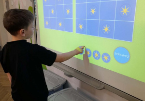 Marcel stoi przed tablicą multimedialną i układa gwiazdki na planszy według podanego wzoru.