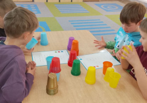 Czterech chętnych chłopców siedzi przy stole i wykonuje działania przedstawione na wybranych przez siebie kartach wzoru. Dzieci ustawiają wieżę według kodu.