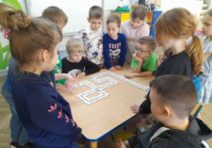 Dzieci z zainteresowaniem oglądają poruszającego się po ułożonej z puzzli trasie Ozobota.