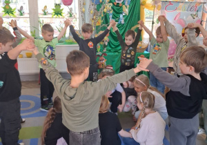 Dzieci tworzą dwa koła: dziewczynki kucają w środku na zewnątrz chłopcy trzymają ręce do góry.