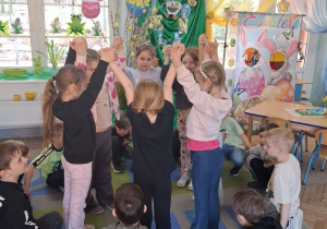 Dzieci tworzą dwa koła: dziewczynki trzymają ręce do góry w środku koła na zewnątrz chłopcy kucają.