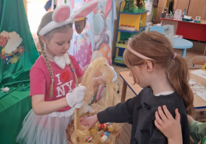 Emma wyjmuje z kosza trzymanego przez koleżankę wielkanocną gniotkę.