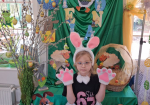 Zuzia w stroju zajączka pozuje do zdjęcia na tle dekoracji.