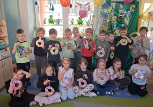 Zdjęcie grupowe na tle dekoracji z wykonanymi wieńcami wielkanocnymi.
