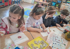 Grupka dzieci koloruje wielkanocną pisankę ze sklejki.