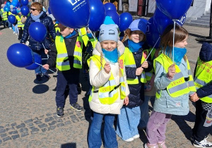 "Słoneczka" idą parami trzymając niebieskie balony.
