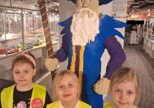 Trzy dziewczynki pozują do zdjęcia na tle budowli przedstawiającej czarodzieja.