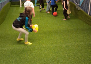 Grupka dzieci gra w piłkę nożną na boisku.