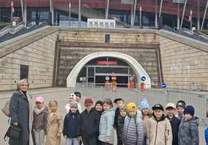 Dzieci razem z Panią dyrektor stoją przed Stadionem Narodowym.