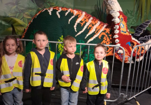 Czworo dzieci stoi przed figurą dinozaura z klocków Lego.