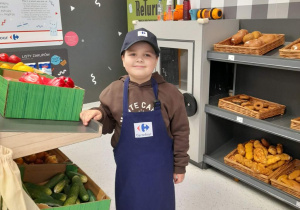 Julek w roli pracownika Carrefoura stoi obok stoiska z warzywami.