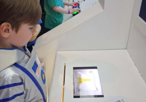 Staś skanuje swoją kosmiczną kolorowankę. W tle kilkoro dzieci podczas gry.