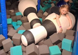 Troje dzieci bawi się w basenie wypełnionym piankowymi kostkami i dmuchanymi kręglami.