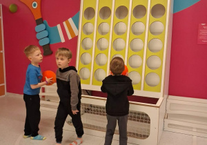 Trzech chłopców rzuca piłki do koszy.