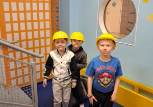 Trzech chłopców stoi obok siebie w kaskach na głowie.