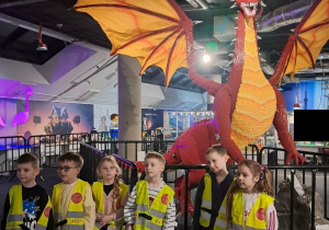 Grupka dzieci stoi przed budowlą z klocków Lego przedstawiającą Czerwonego Smoka.