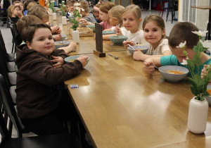 Dzieci siedzą przy wspólnym stole podczas obiadu i jedzą zupę.