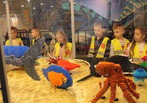 Grupka dzieci ogląda figury ryb w klocków Lego.