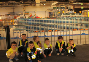 Grupka dzieci przykucnęła pozując do zdjęcia na tle statku pasażerskiego z klocków Lego.