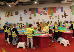 Dzieci stoją przy dwóch stołach i tworzą własne konstrukcje z klocków.