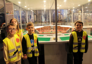 Czworo dzieci stoi na tle Stadionu Narodowego z klocków Lego.