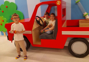 Marysia i Staś siedzą w ciężarówce, a obok stoi Mikołaj z jabłkiem w ręku.