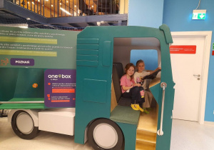 Emma i Nikola podczas zabawy w strefie "Zgrana paczka" siedzą w dostawczej ciężarówce.