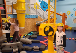 Mateusz stoi obok dźwigu na placu budowy.