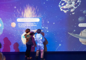 Julek i Staś obserwują lot obrazka przedstawiającego rakietę na interaktywnej ścianie.