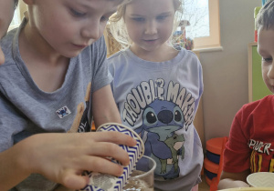 Olek wlewa wodę do przezroczystego kubeczka, w którym znajduje się Pani Greenie.