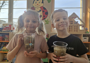 Liliana i Marcel trzymają w dłoniach przezroczyste kubki z zanudzonymi zabawkami Pani Greenie.