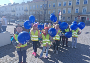 Dzieci z grupy Biedronek idą w marszu trzymając w dłoniach niebieskie balony.