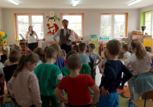 Dzieci śpiewają piosenkę powitalną, a przed nimi stoi Pan prowadzący audycję muzyczną oraz Pani wokalistka.