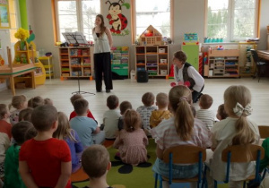 Pani wokalistka stoi przed dziećmi i prezentuje śpiew klasyczny.