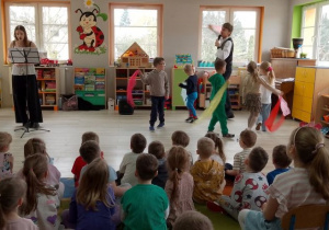 Pani wokalistka śpiewa, a dzieci idą w kole poruszając kolorowymi chustkami. Razem z dziećmi bawi się Pan prowadzący zajęcia.