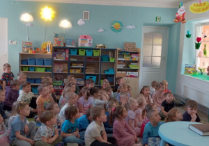 Pani stoi obok stolika, na którym leży książka dla osób niewidomych i opowiada dzieciom o alfabecie Braille’a.