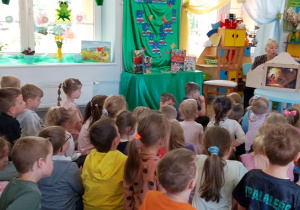 Dzieci siedzą na dywanie, a Pani z biblioteki czyta przedszkolakom bajkę zaprezentowaną w Teatrzyku Kamishibai pt. Amelka i latająca księga".