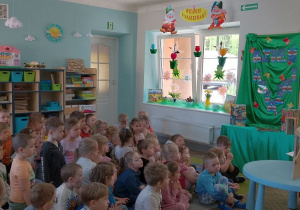 Dzieci siedzą na dywanie, a przed nimi Pani z biblioteki czyta bajkę zaprezentowaną w Teatrzyku Kamishibai