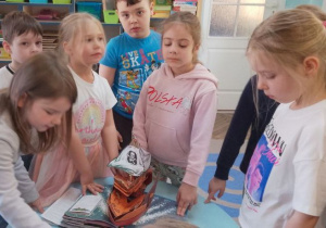 Grupa dzieci stoi przy stoliku i ogląda przestrzenną ilustrację w książce pt. "Piotruś Pan".